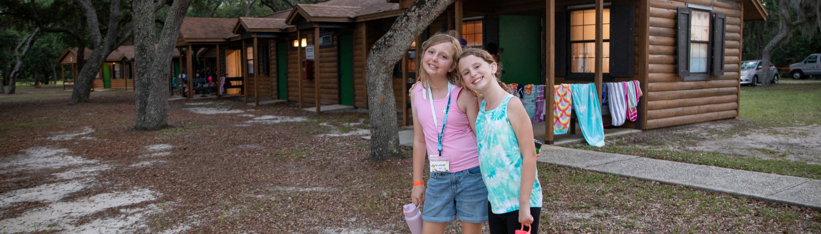 Banner image of 2 youth smiling in front of the cabins at camp timpoochee