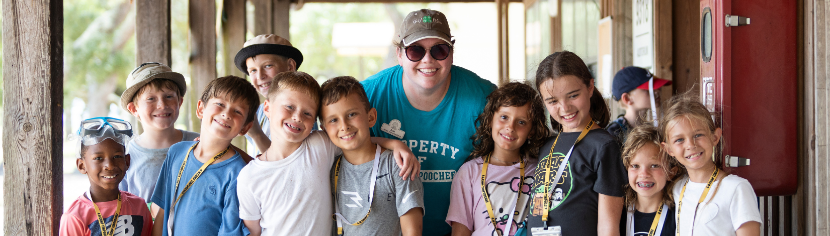 Group of children with a camp director at a summer camp, smiling and posing for a photo.