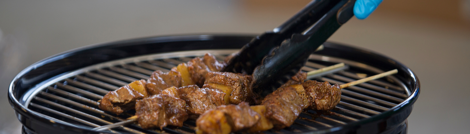 Banner image of someone grilling kebabs